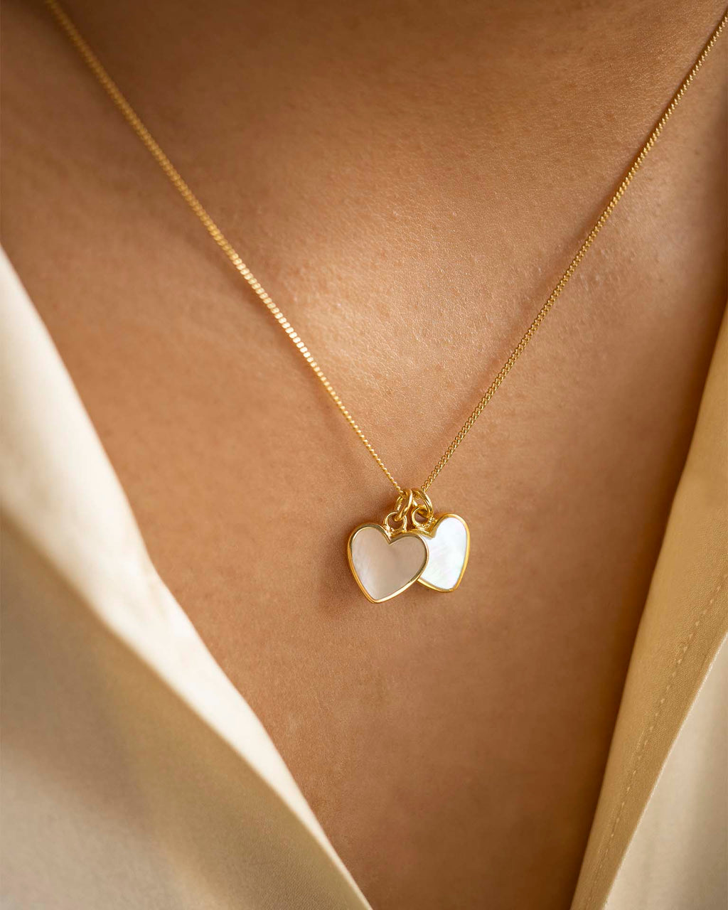 Gold necklace with heart-shaped pendants on a person wearing a white garment.