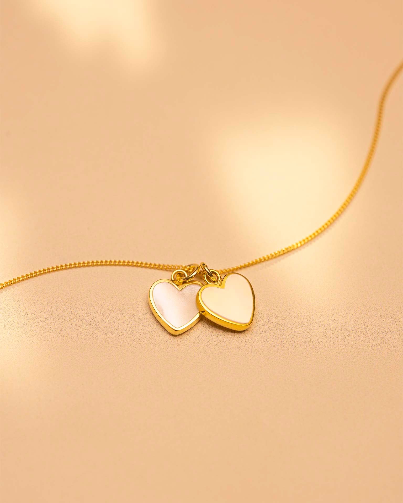 Gold necklace with heart-shaped pendants on a beige background