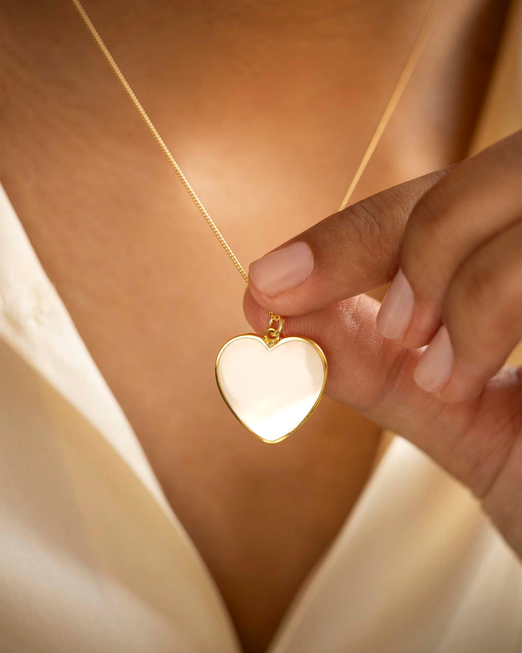 Heart-shaped gold pendant held by a hand against a soft background