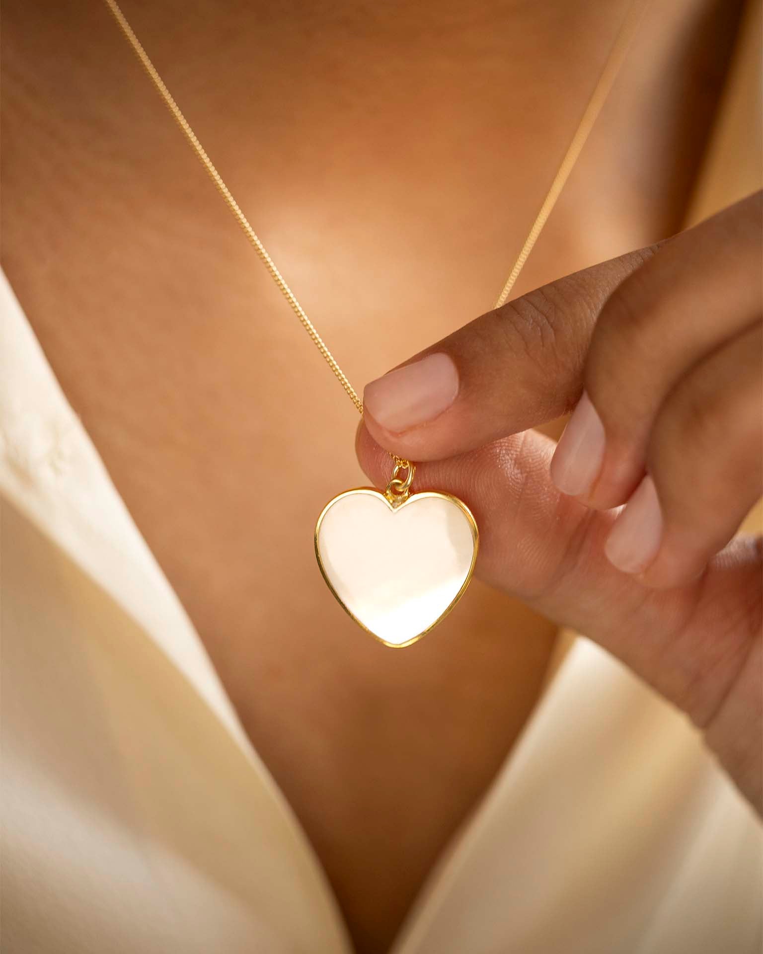Heart-shaped gold pendant held by a hand against a soft background
