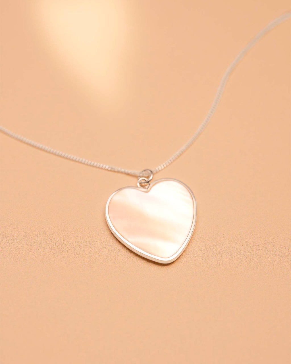 Heart-shaped silver pendant on a beige background