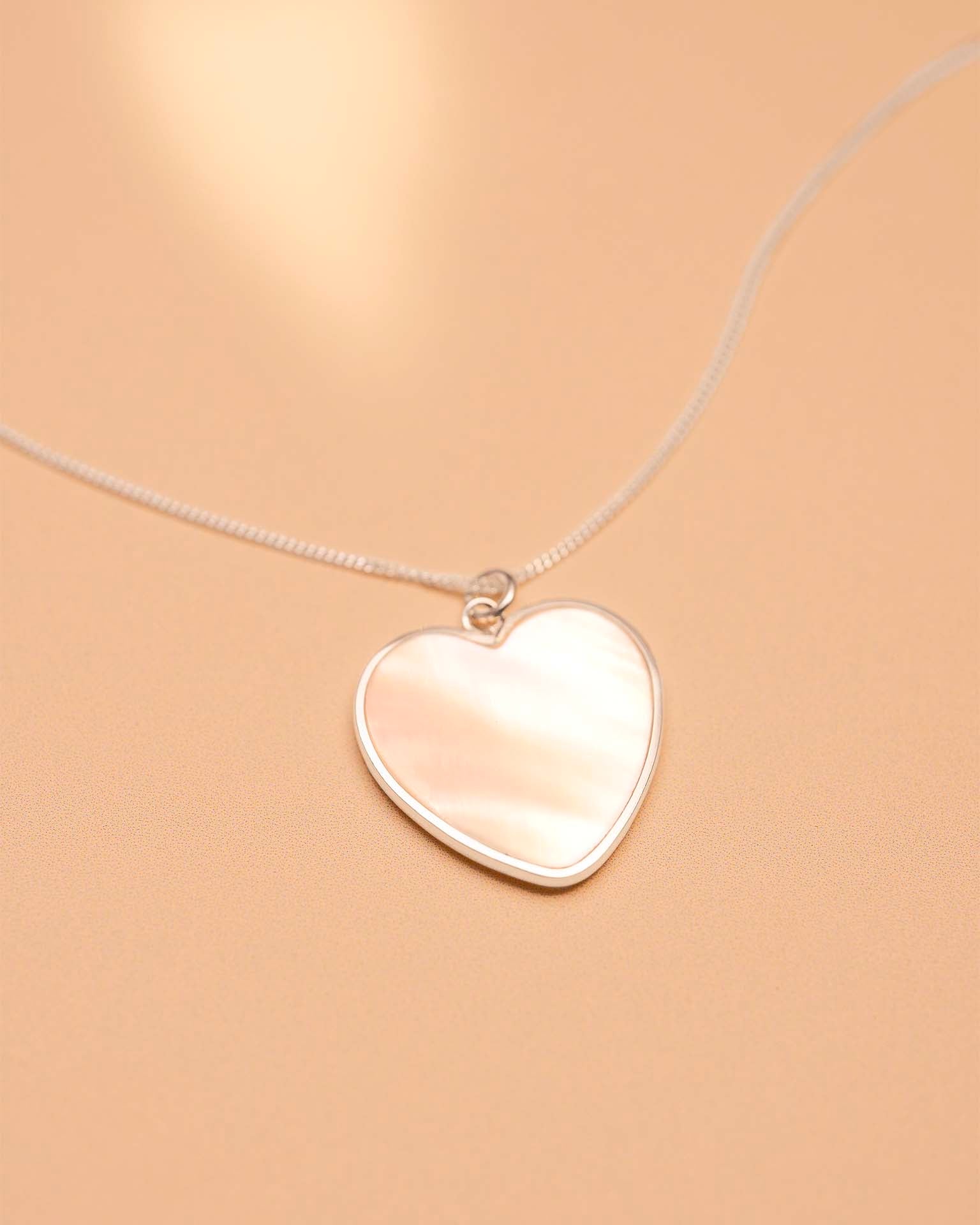 Heart-shaped silver pendant on a beige background