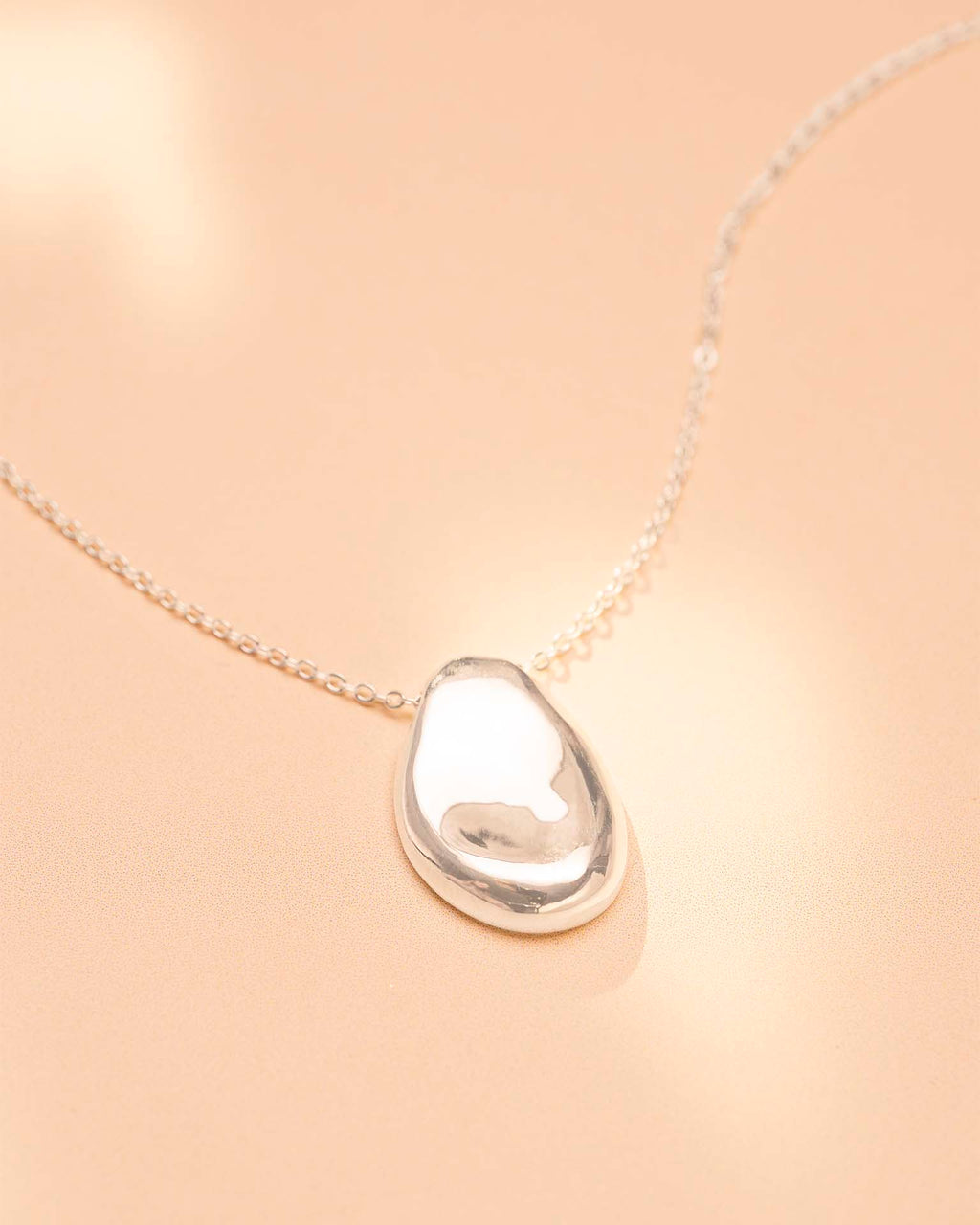Teardrop-shaped silver pendant on a beige background