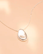 Teardrop-shaped silver pendant on a beige background