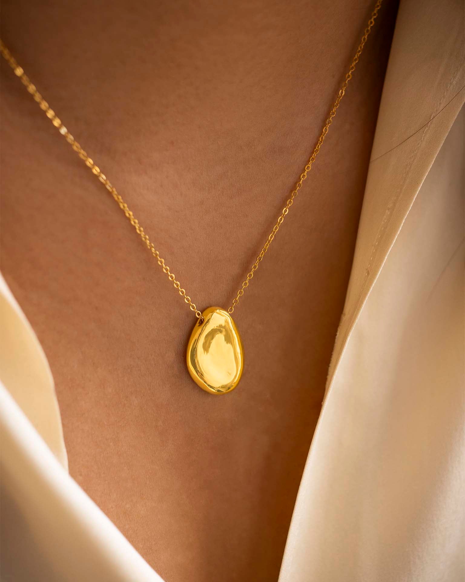 Gold necklace with a teardrop-shaped pendant on a neutral background