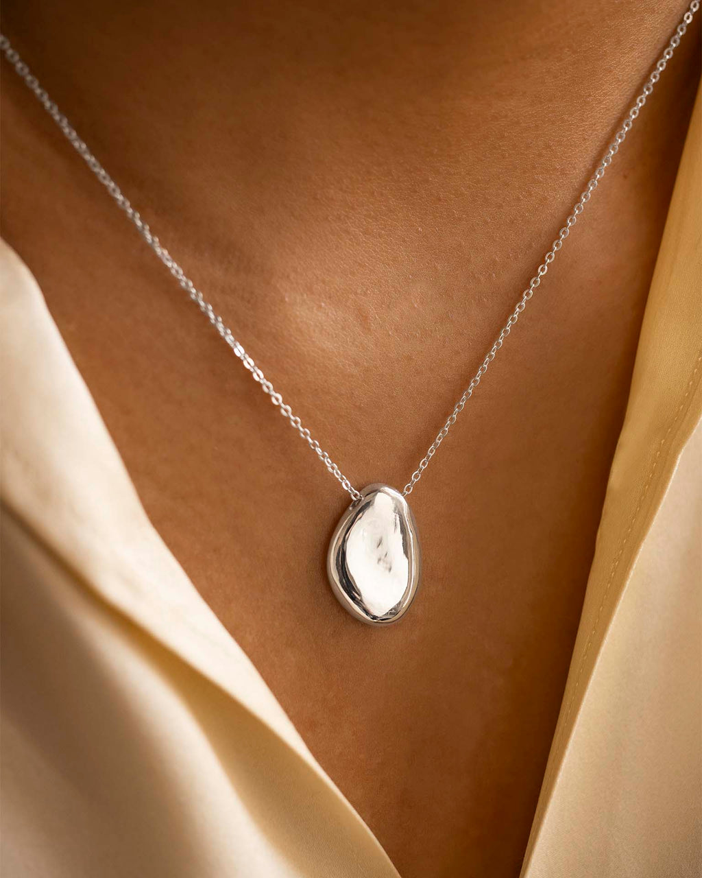 Silver necklace with a pendant on a person wearing a beige garment