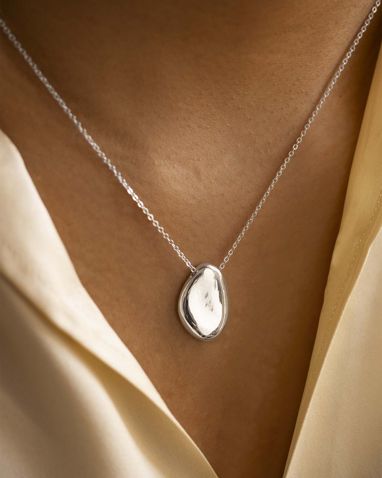 Silver necklace with a pendant on a person wearing a beige garment