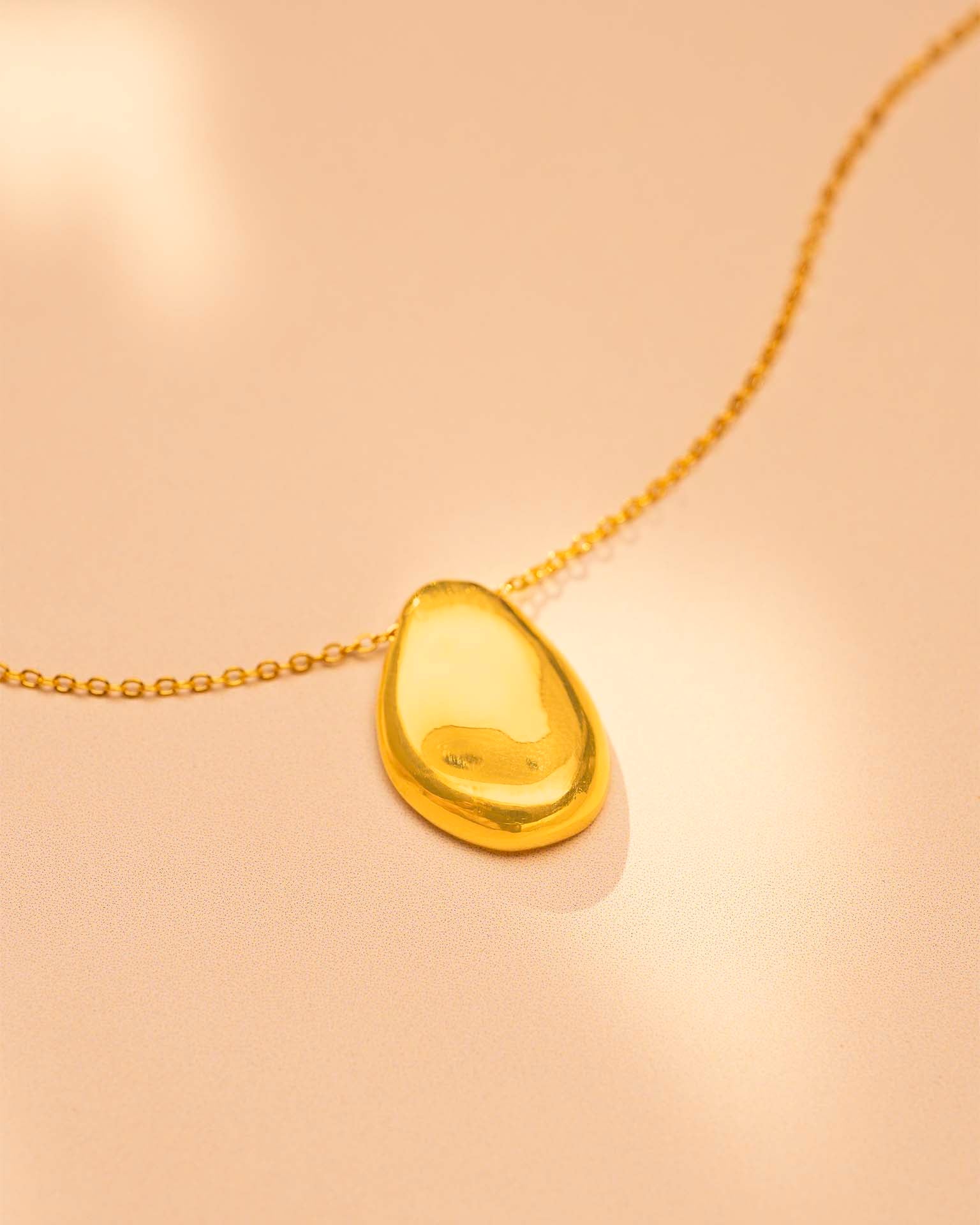 Gold pendant on a beige chain against a beige background