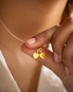 Gold necklace with heart-shaped pendants held by a hand against a neutral background