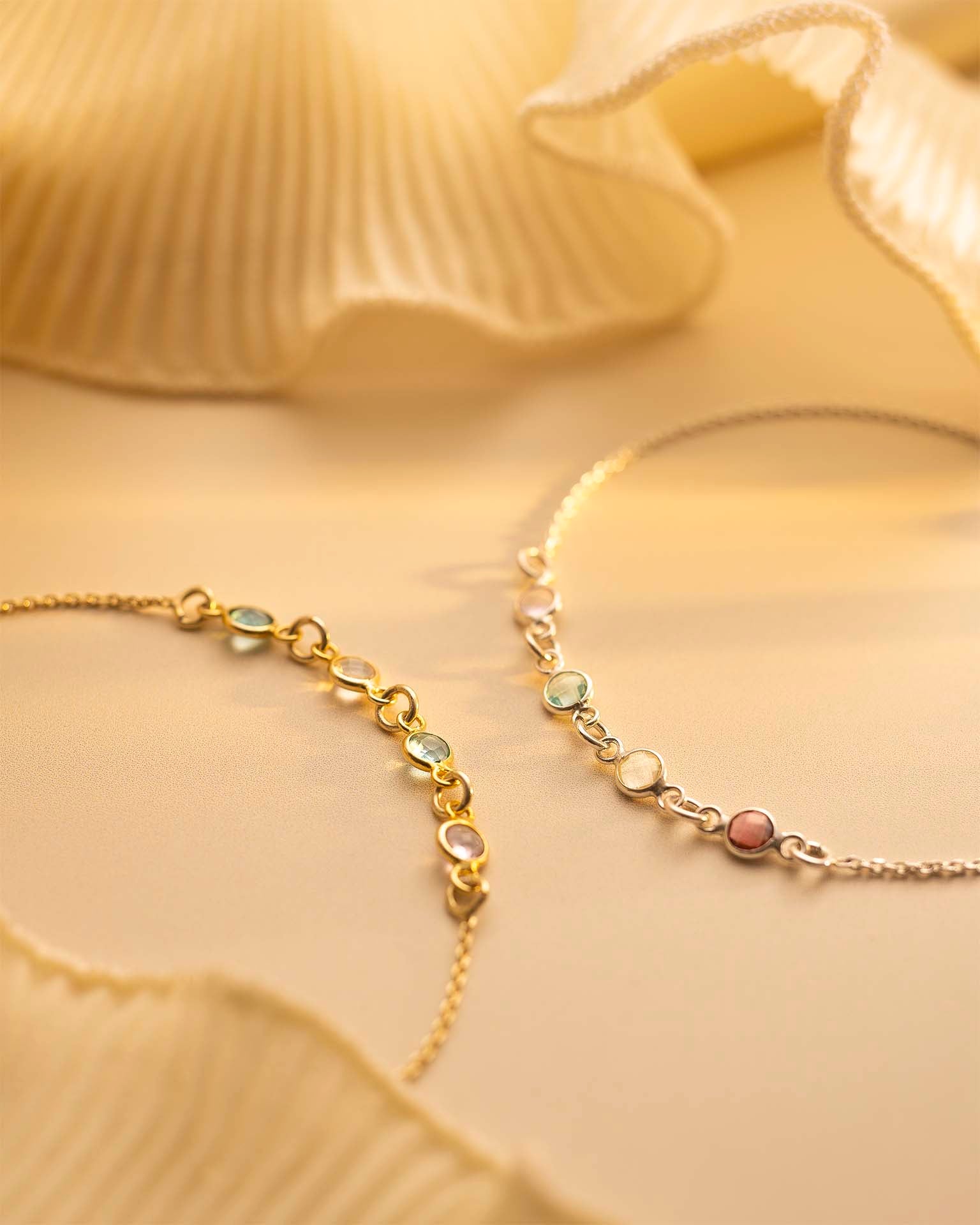 Gold bracelet with small colored stones on a soft yellow fabric background