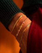 Gold bracelets with gemstones on a wrist against a blurred background