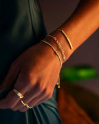 Close-up of a hand wearing gold bracelets and rings against a blurred background