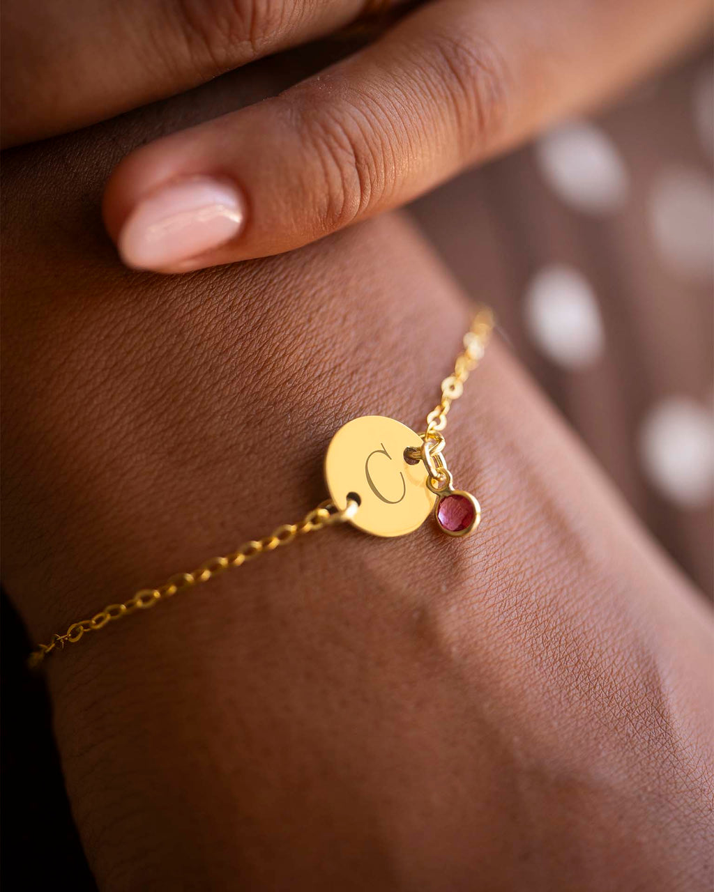 Gold bracelet with a round charm and red gemstone on a wrist. | Christmas