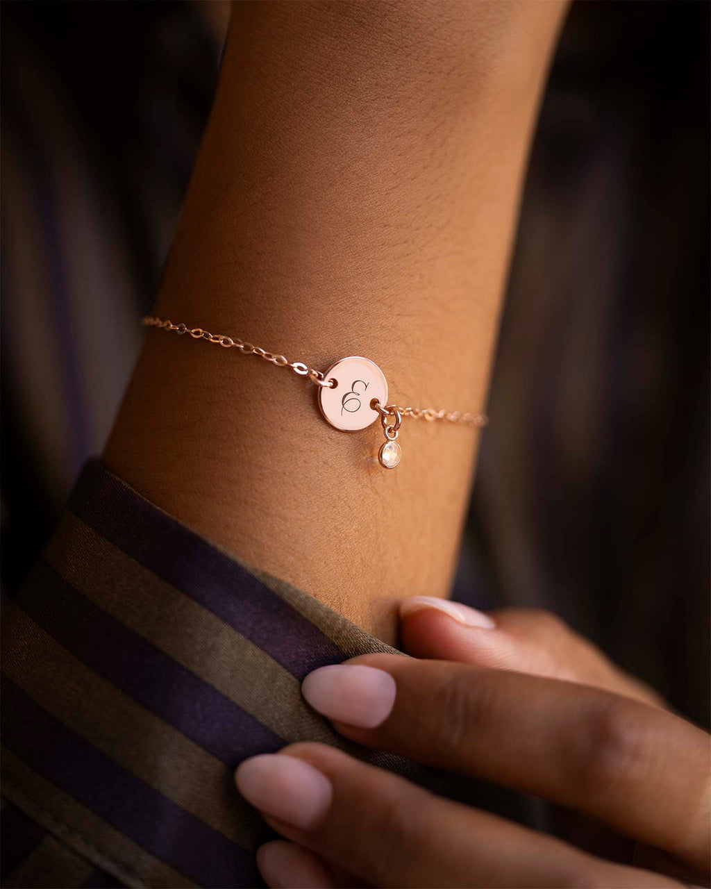 Rose gold bracelet with a heart charm on a wrist against a dark background