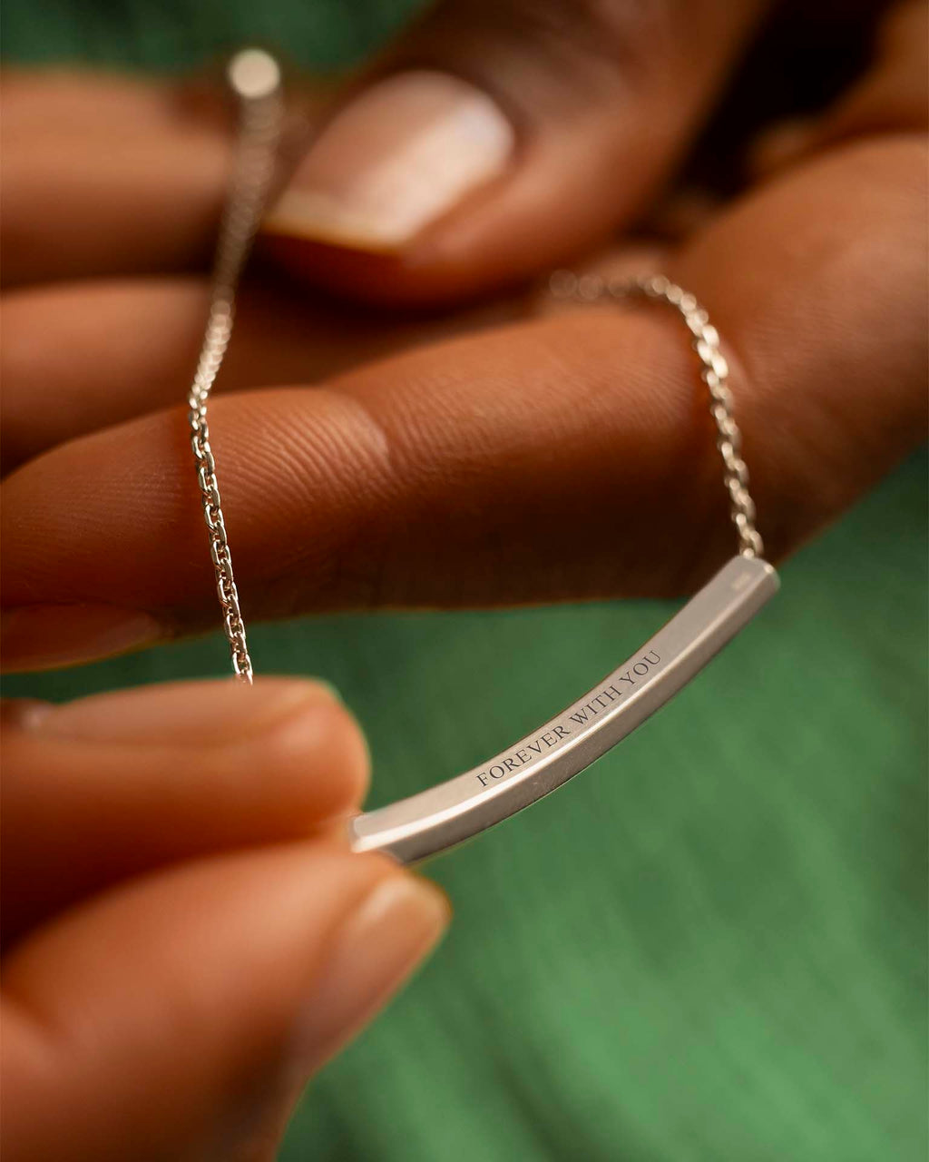 Silver bracelet with 'Forever With You' engraving held by a hand against a green background | 
Christmas