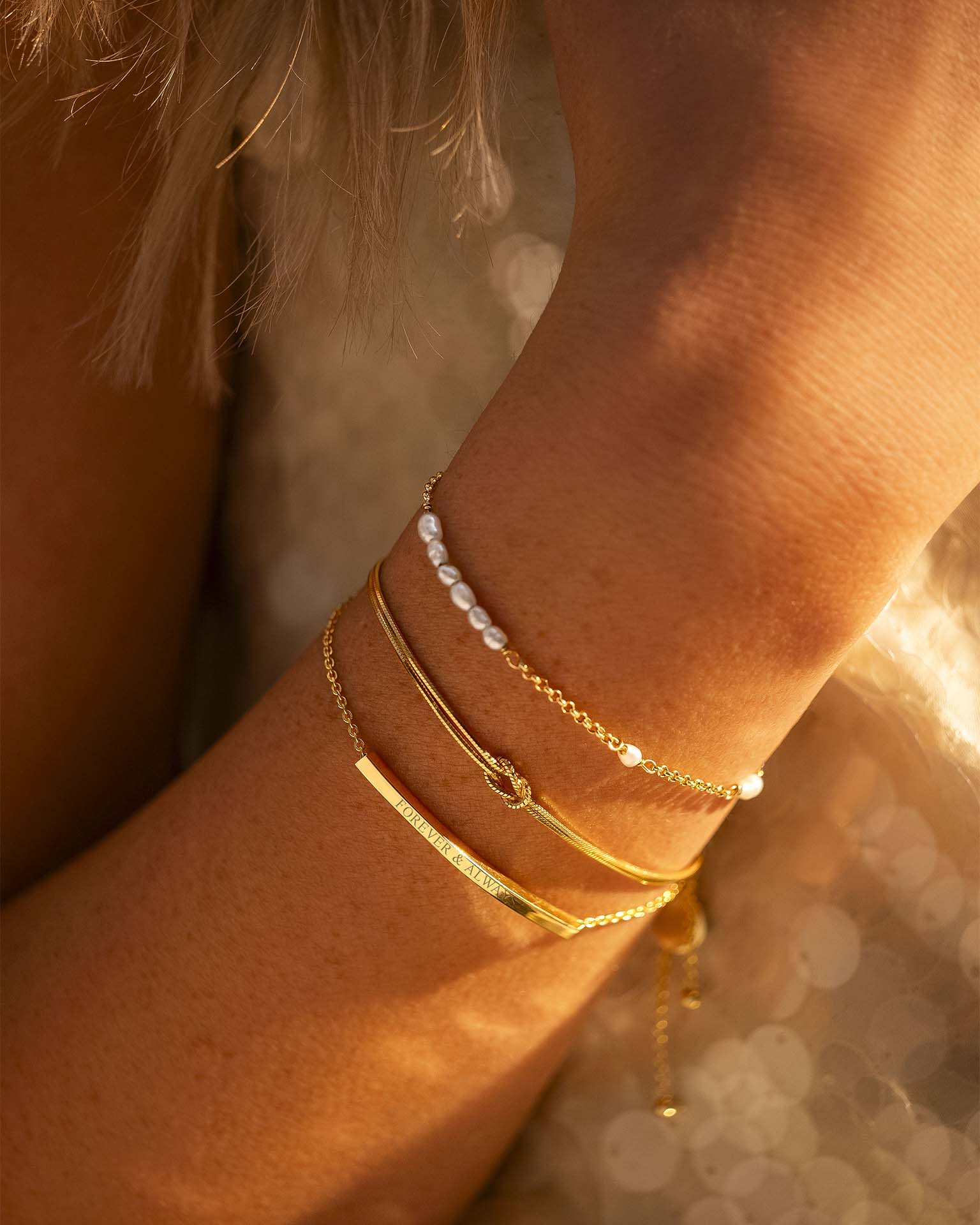 Close-up of a wrist wearing multiple gold bracelets with a blurred background