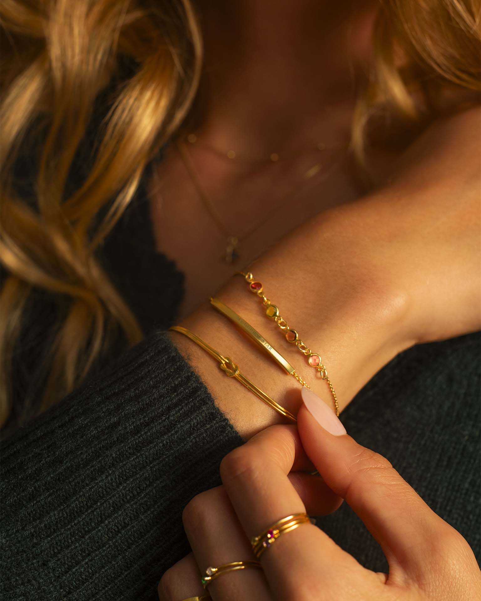 Close-up of a person wearing gold jewelry including bracelets and rings.