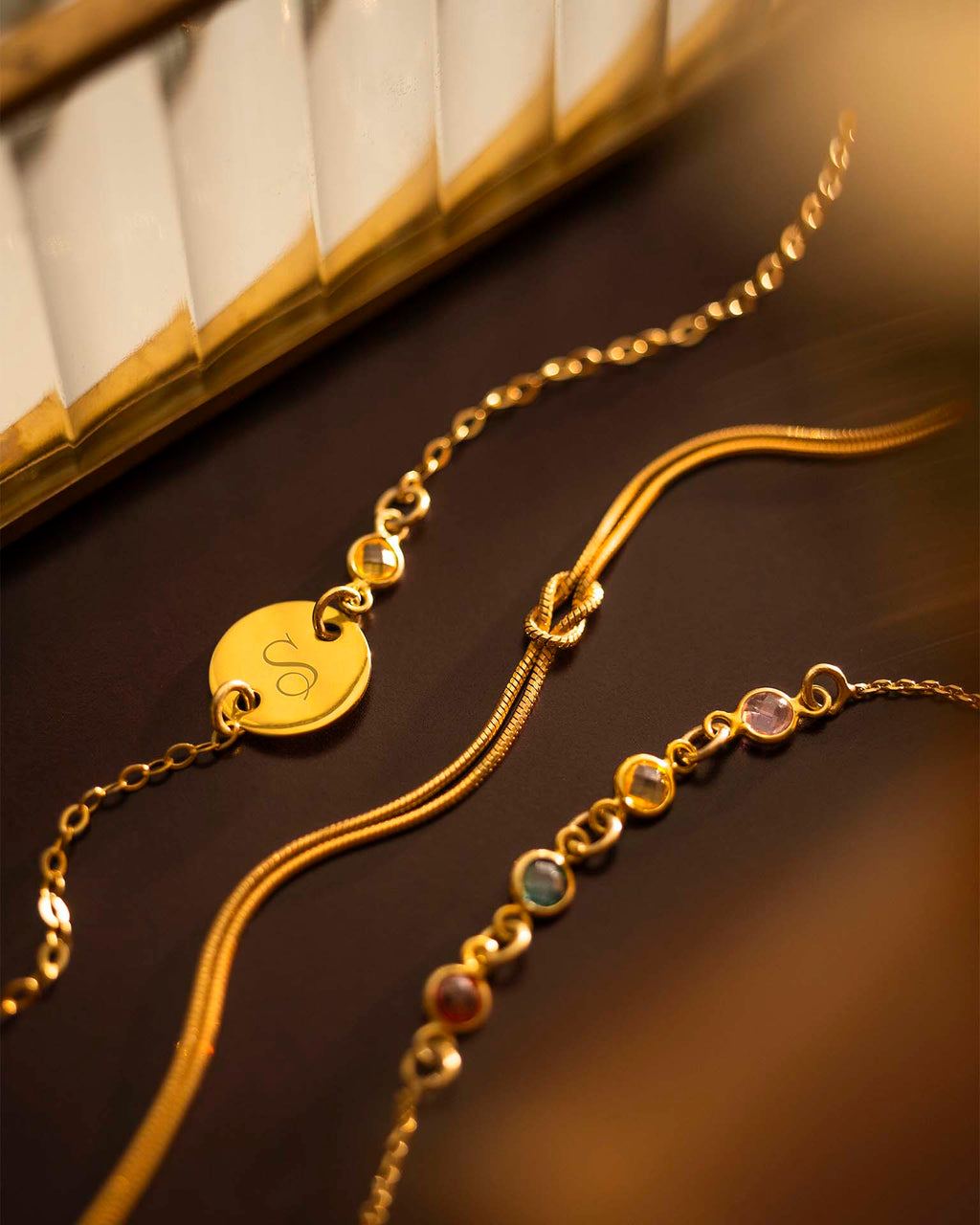 Two gold bracelets with heart-shaped charm and beaded design on a dark surface.