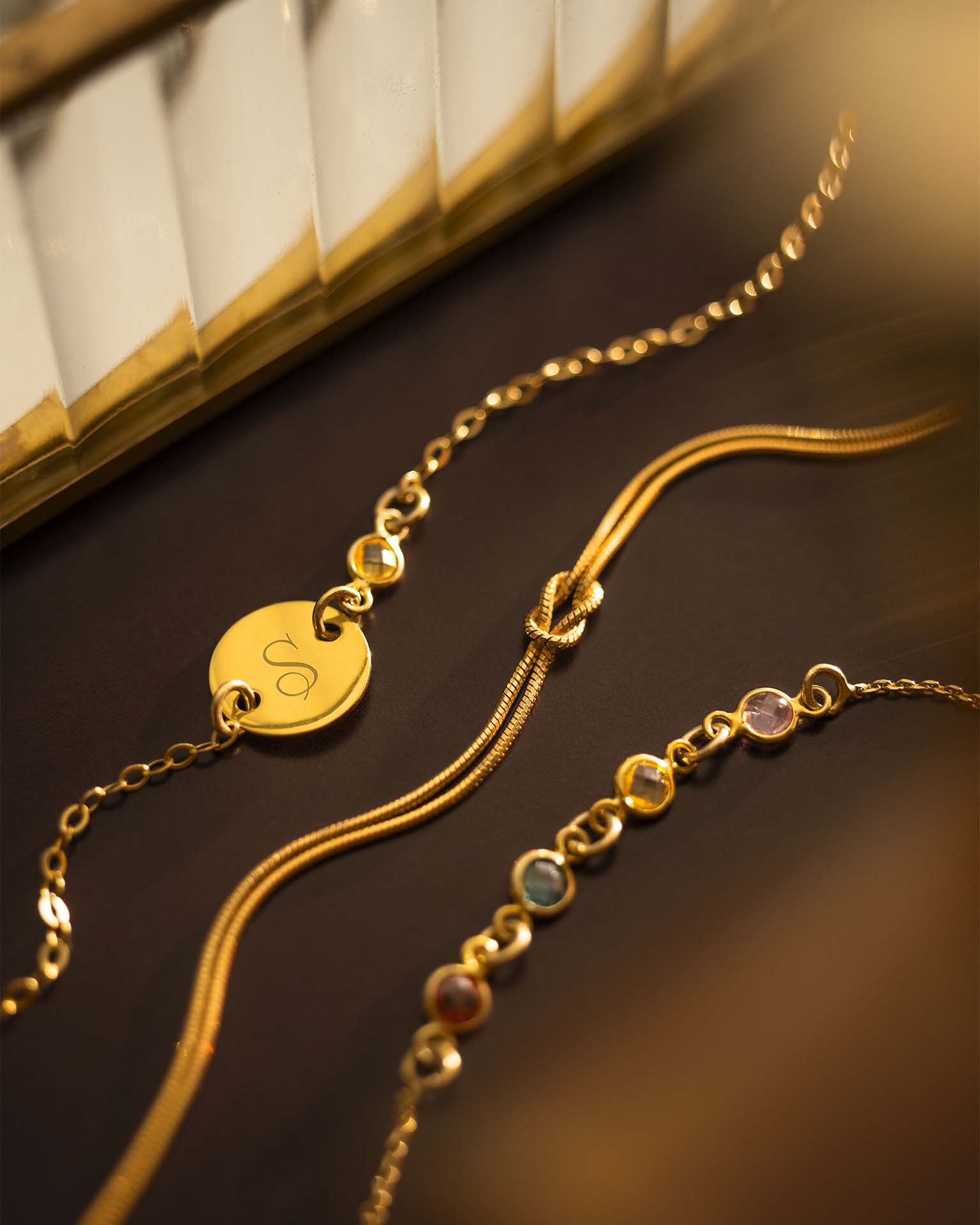 Two gold bracelets with heart-shaped charm and beaded design on a dark surface.