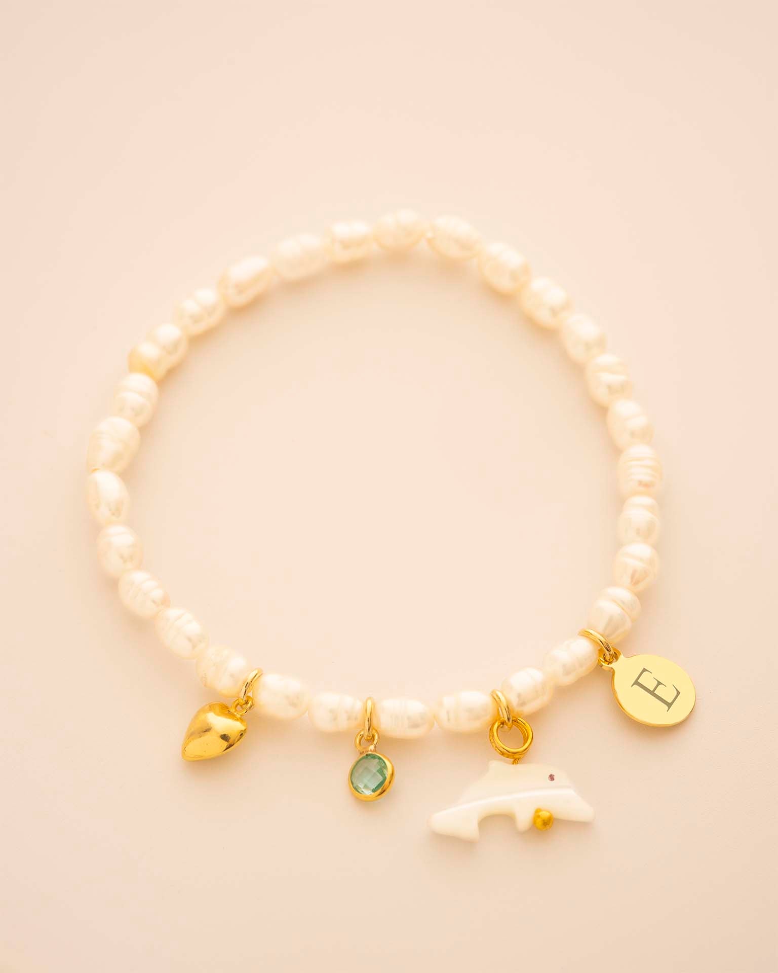Pearl bracelet with gold charms on a beige background 