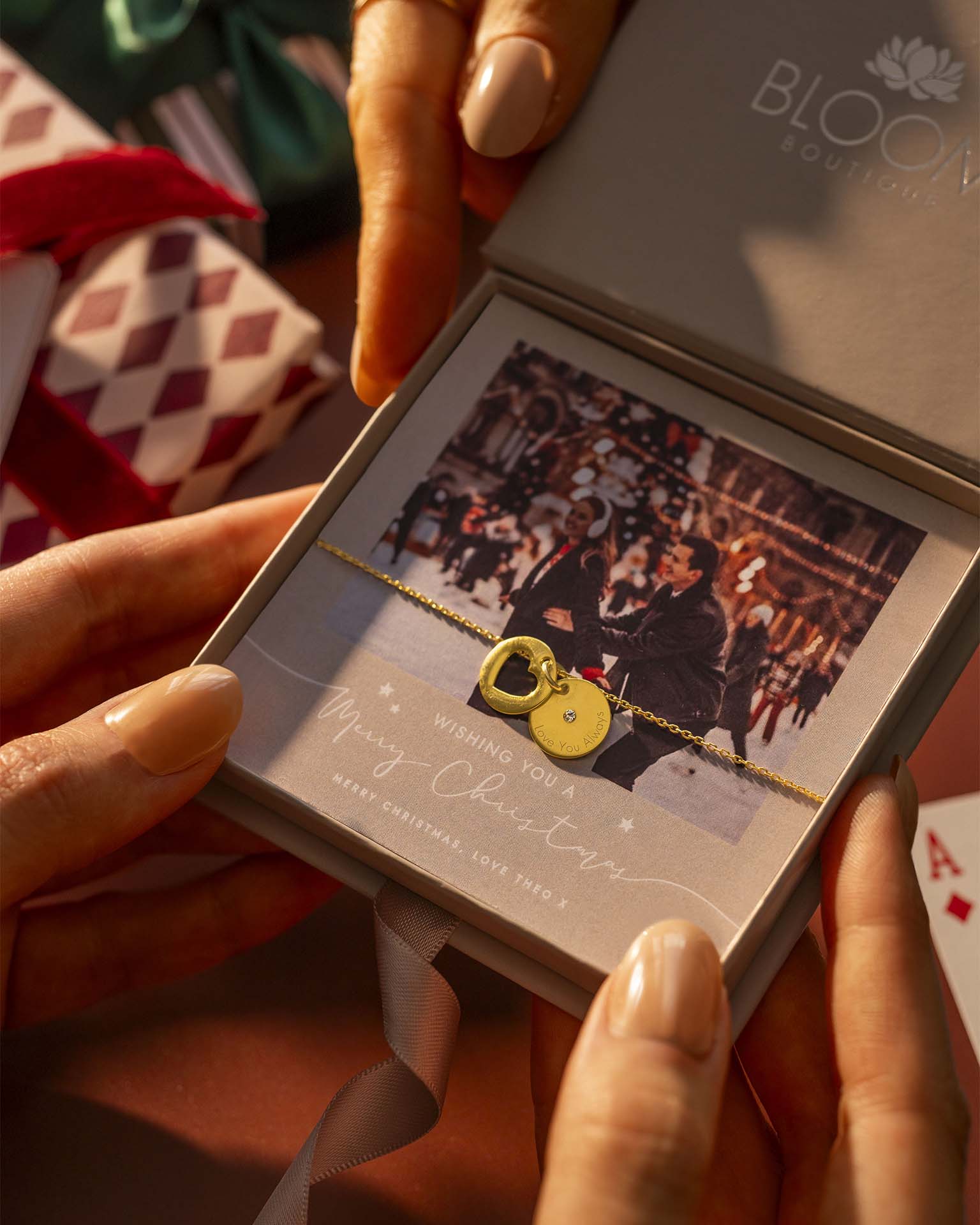 Person holding a jewelry box with a heart-shaped pendant, surrounded by festive decorations.