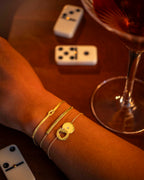 Gold bracelets on a wrist with a glass of red wine and dominoes in the background