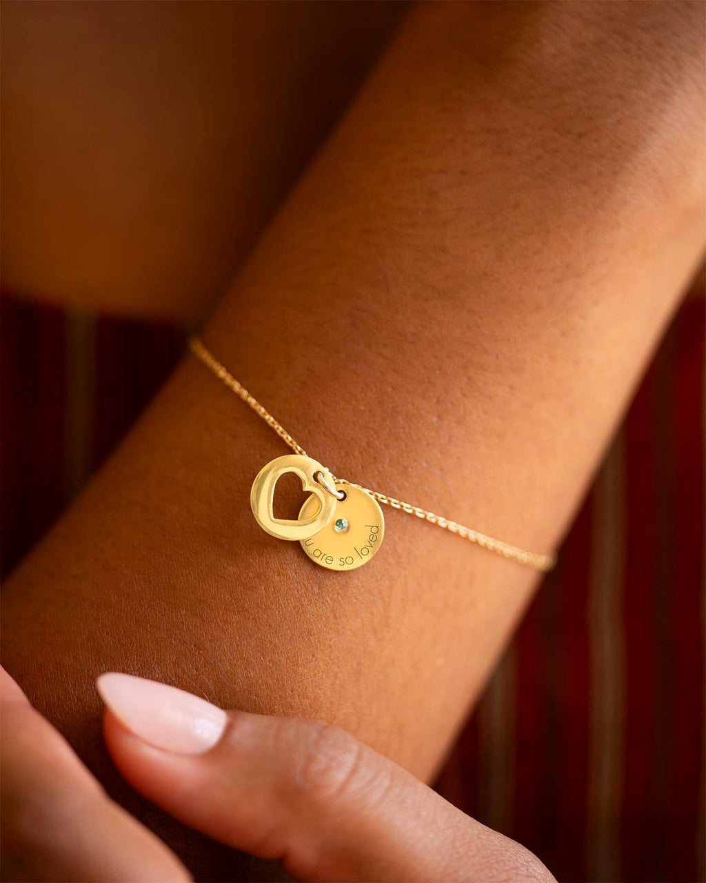 Gold bracelet with heart and round charm on a wrist against a blurred background | Christmas
