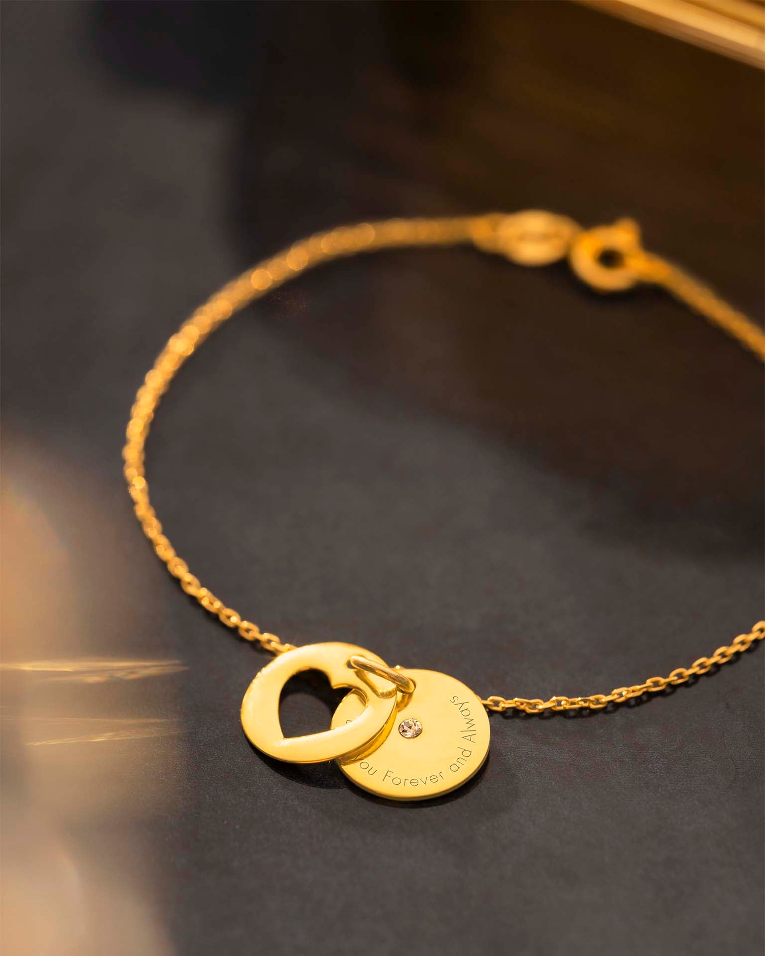 Gold bracelet with two heart-shaped charms on a dark surface