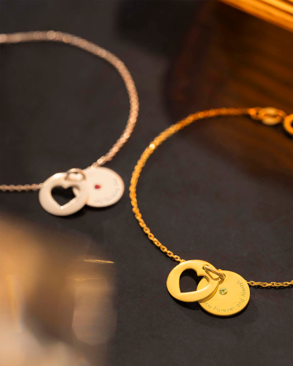 Two gold necklaces with heart-shaped pendants on a dark background