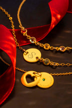 Gold necklaces with heart and round pendants on a dark surface with red ribbons.