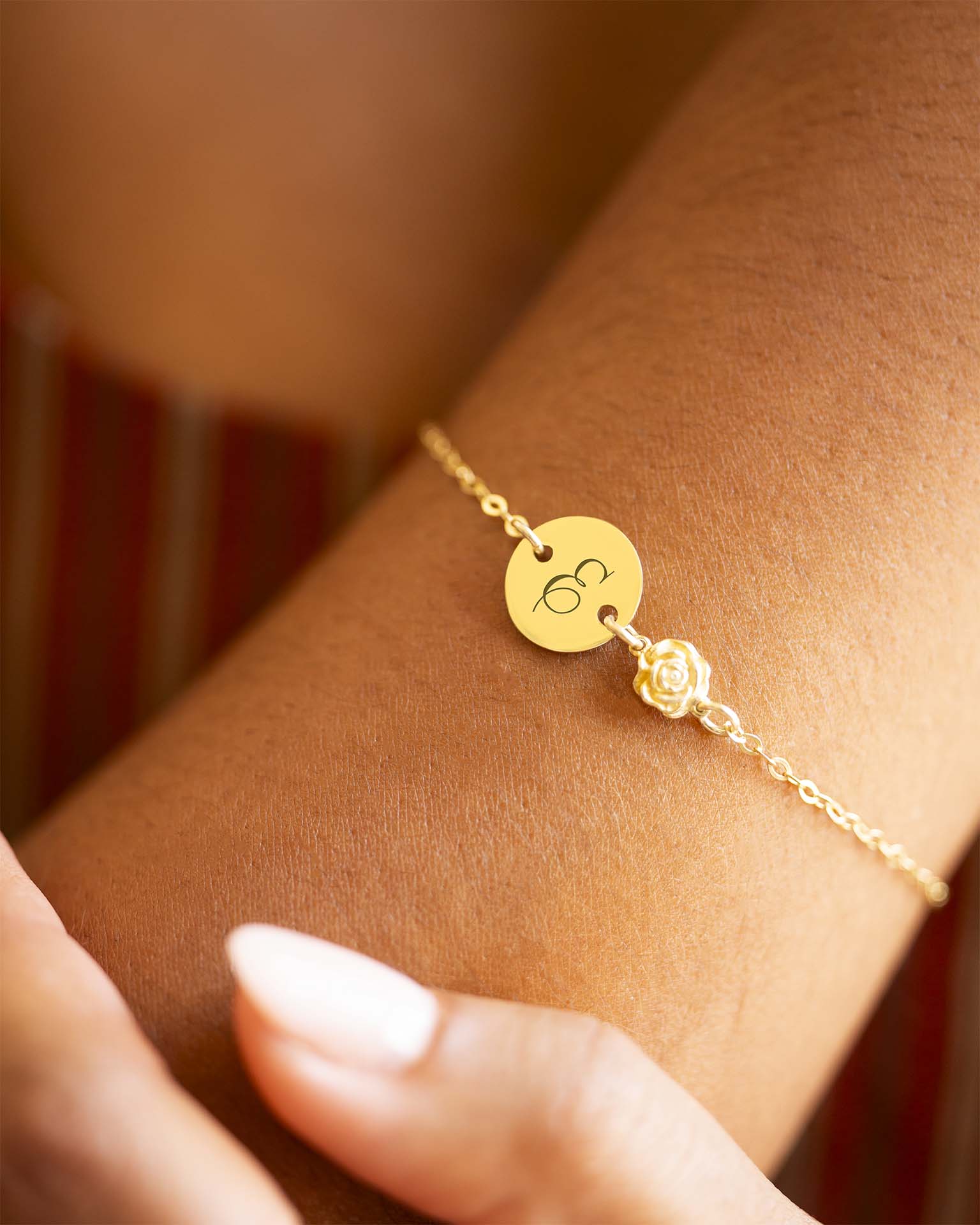 Gold bracelet with a round tag and rose charm on a wrist. | Christmas
