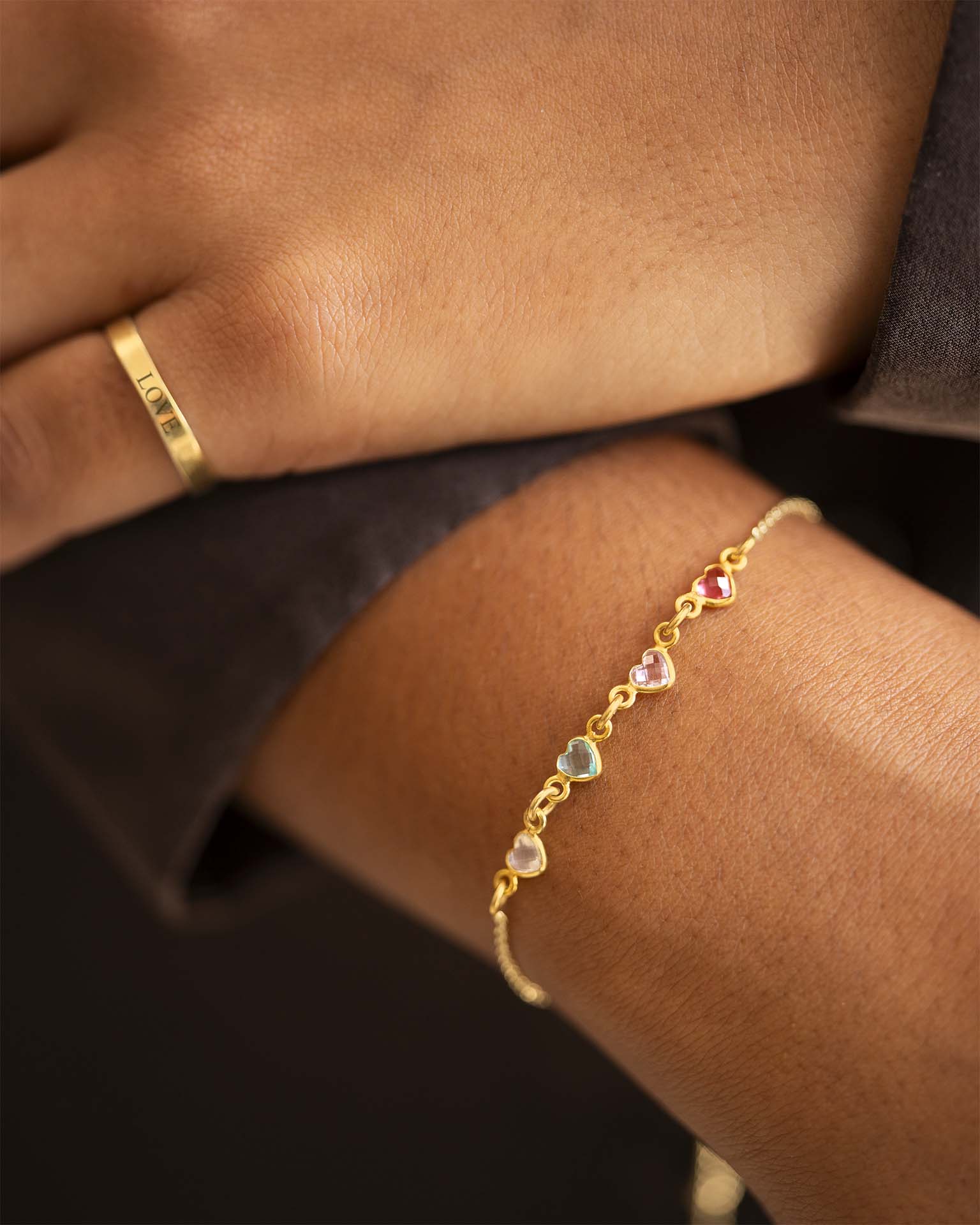 Gold bracelet with heart-shaped gemstones on a wrist, with a gold ring on a finger. | Christmas