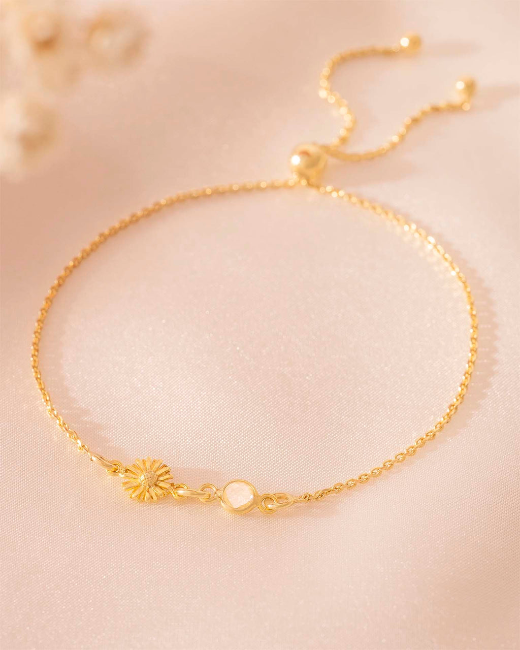 Gold bracelet with a sunflower charm on a beige background