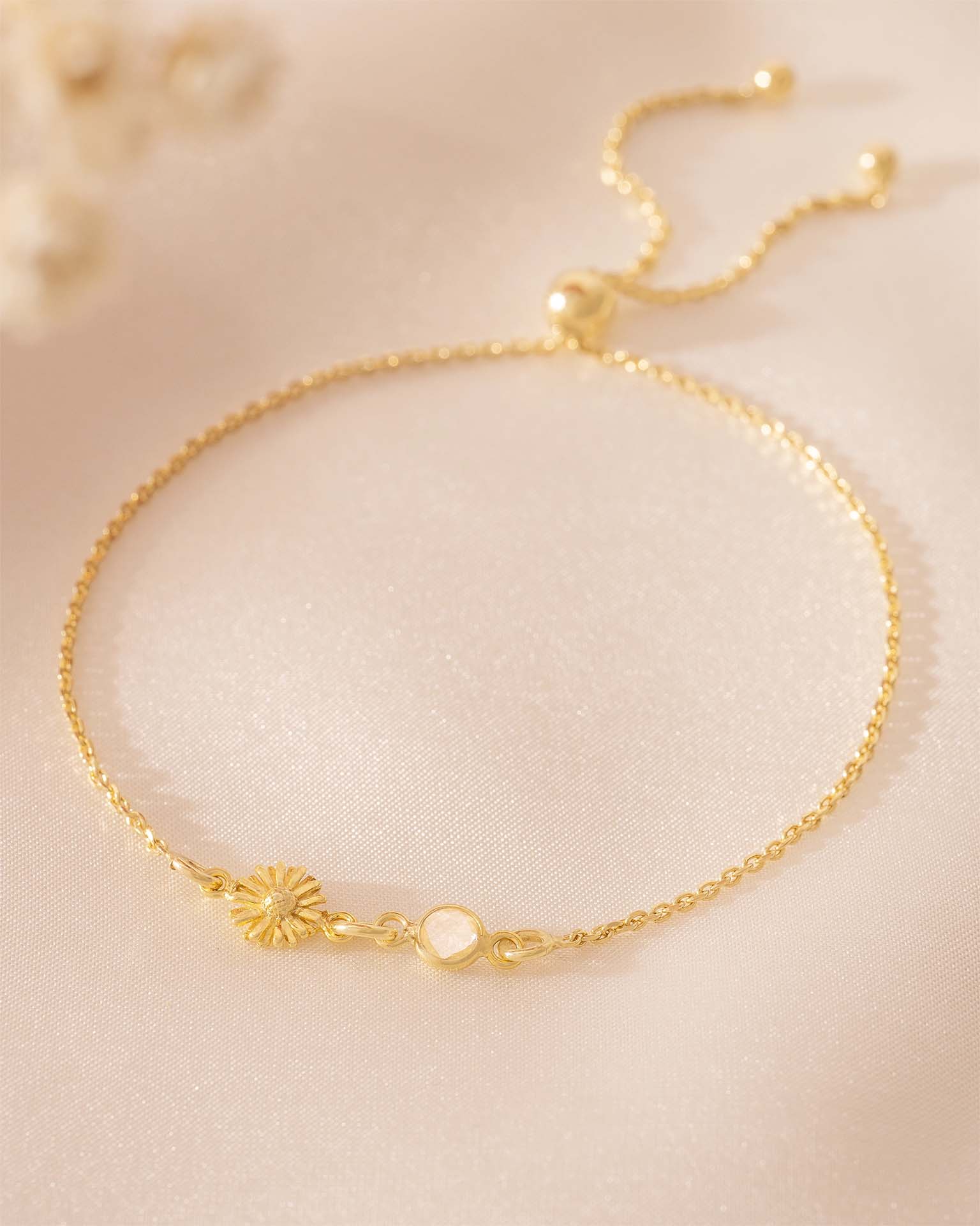 Gold bracelet with a sunflower charm on a beige background