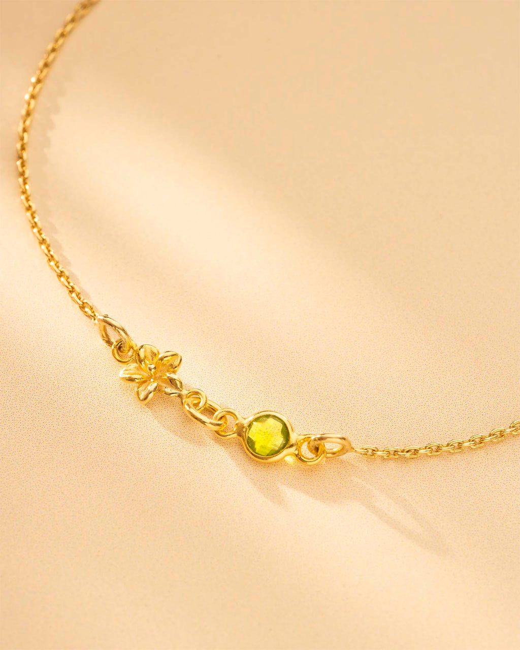 Gold necklace with a green gemstone on a beige background