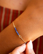 Gold bracelet with blue beads on a wrist against a striped background | Christmas