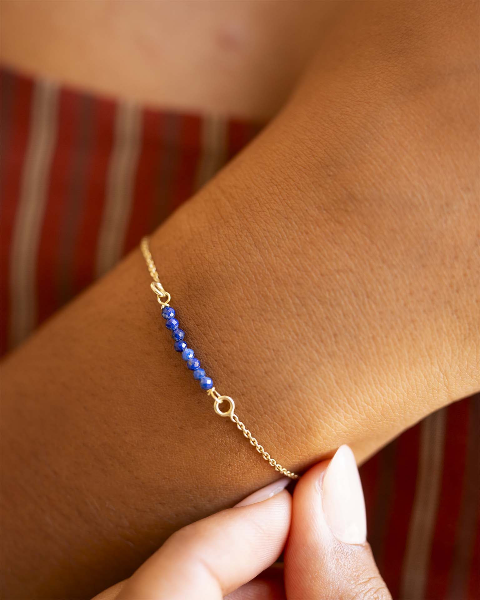 Gold bracelet with blue beads on a wrist against a striped background | Christmas
