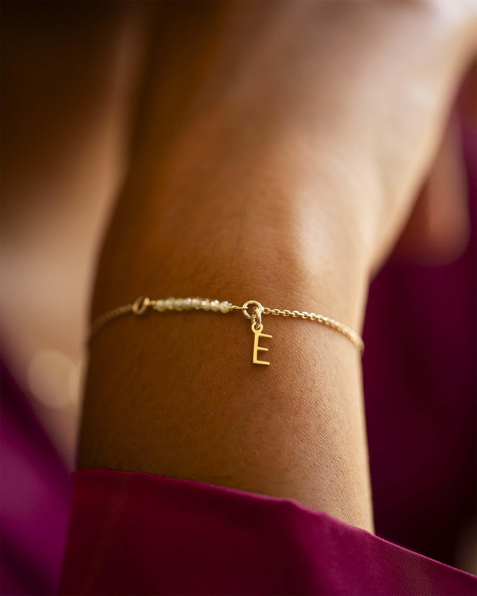 Gold bracelet with a letter 'E' charm on a wrist against a blurred background | Christmas
