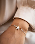 Silver star bracelet on a wrist with a neutral background