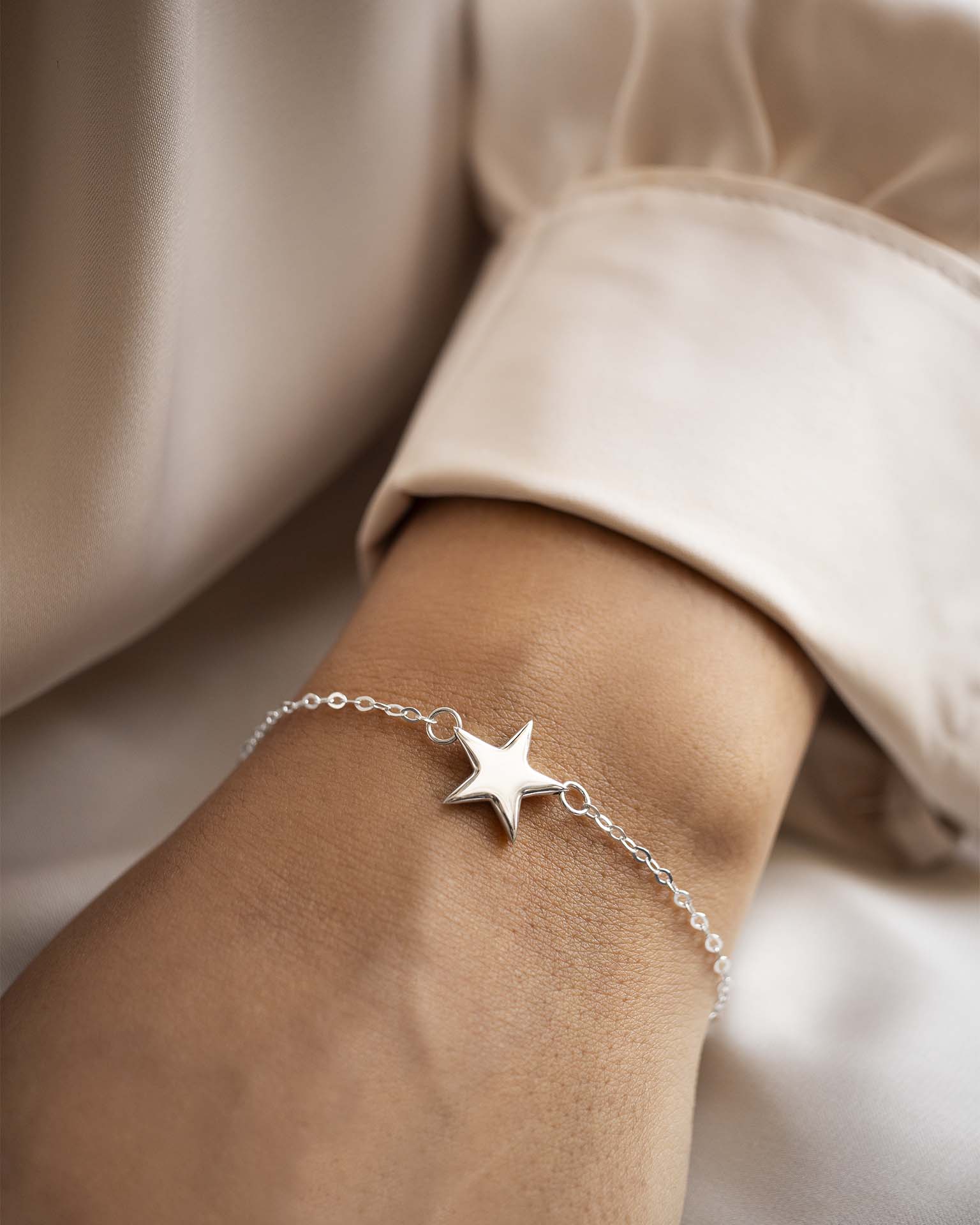 Silver star bracelet on a wrist with a neutral background