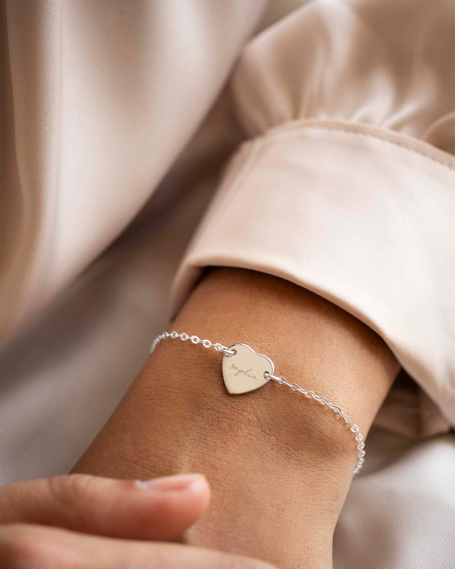 Silver bracelet with a heart-shaped tag on a wrist against a neutral background