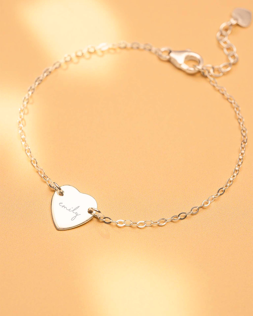 Silver bracelet with a heart-shaped tag on a gold background
