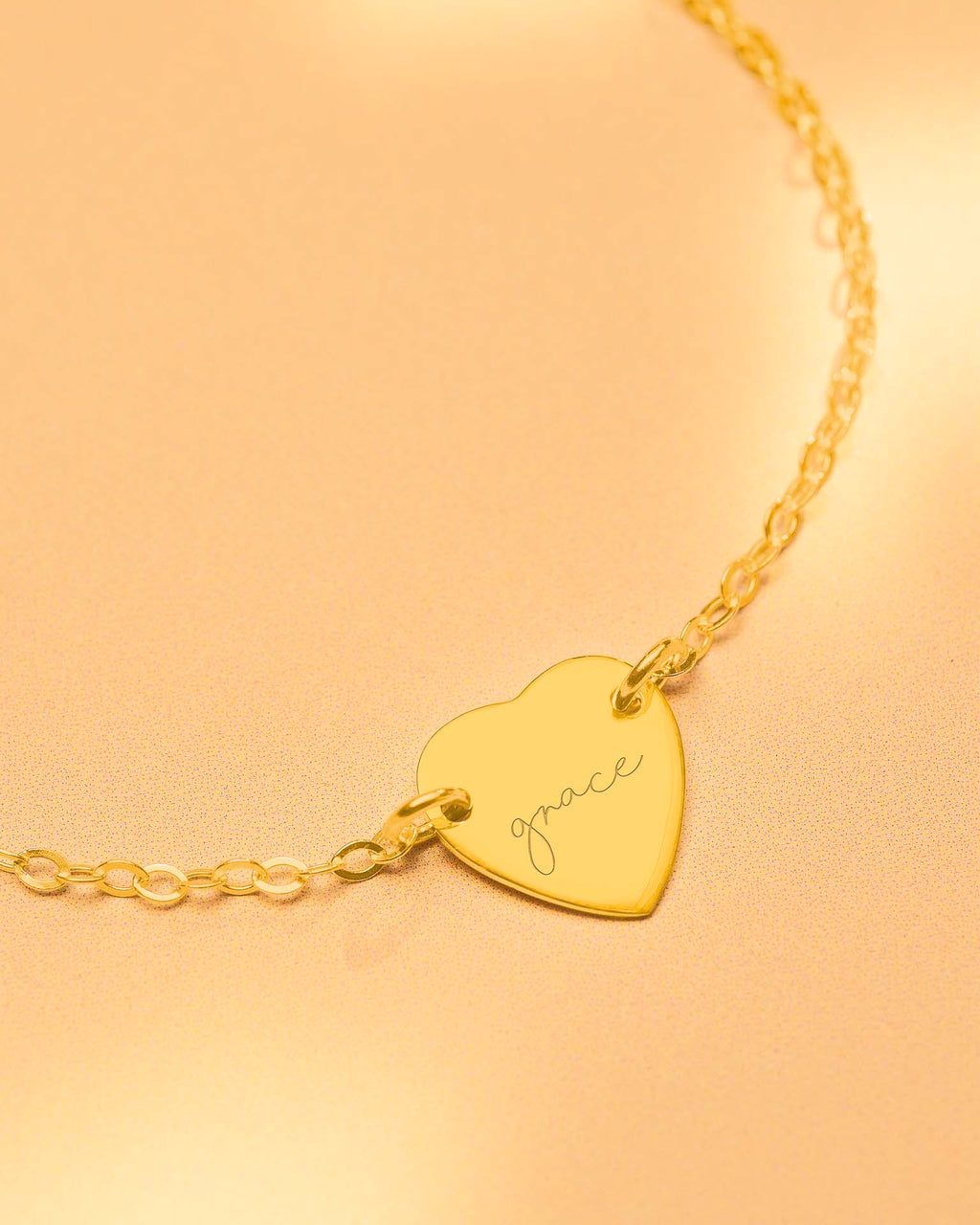 Gold heart-shaped bracelet with 'grace' engraving on a beige background