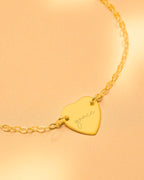 Gold heart-shaped bracelet with 'grace' engraving on a beige background