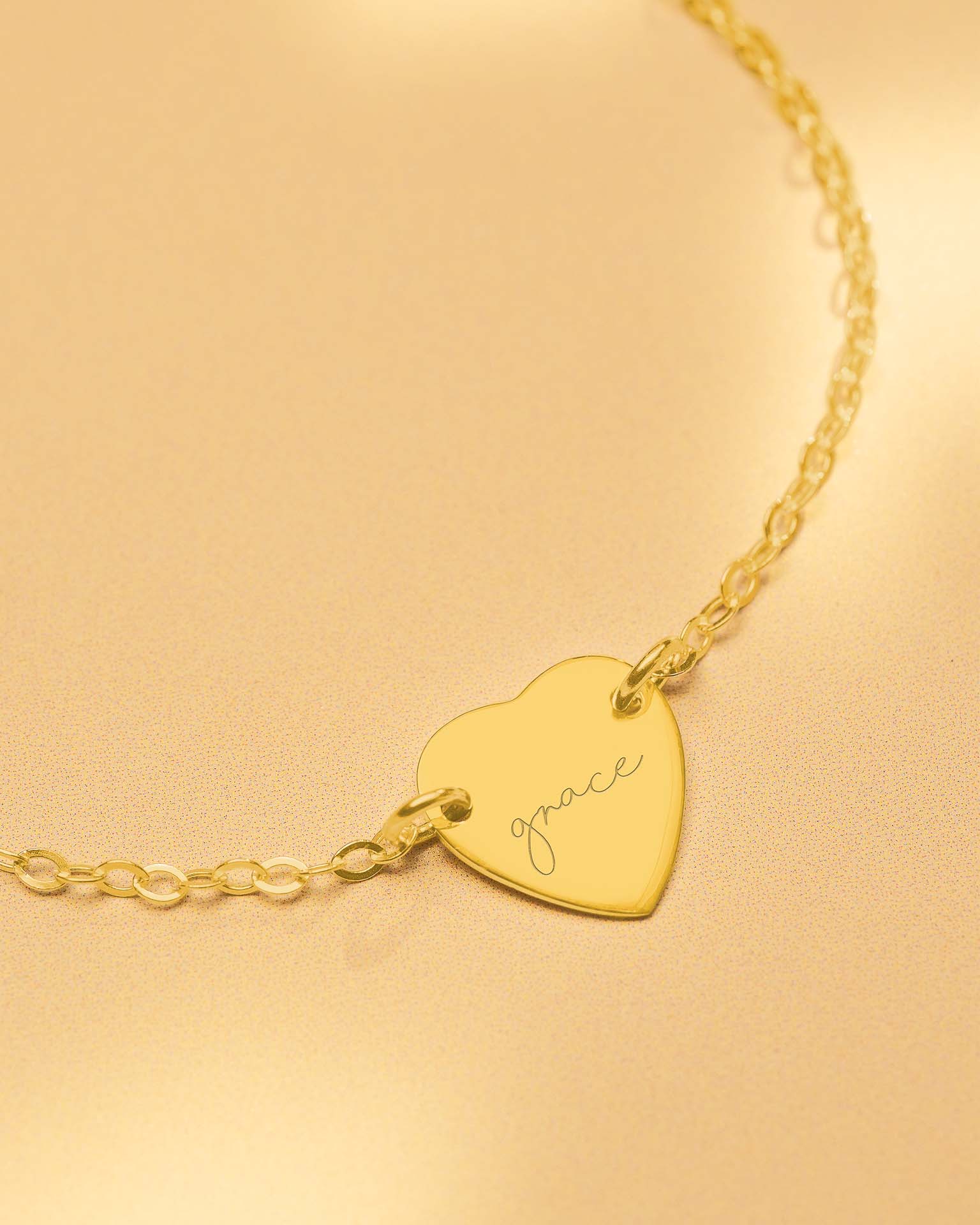 Gold heart-shaped bracelet with 'grace' engraving on a beige background