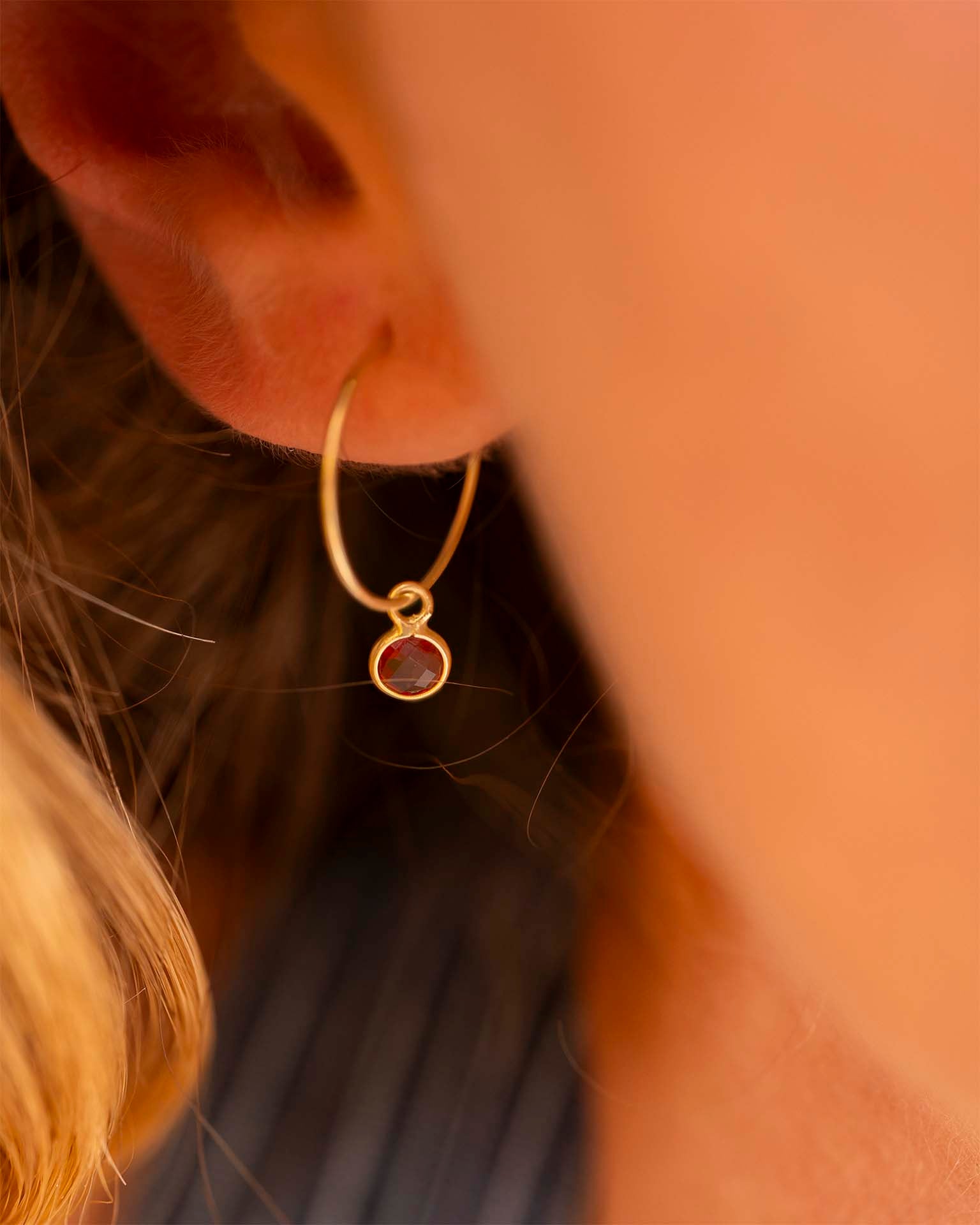 Model with gold earring with red stone and blurred background. | Christmas