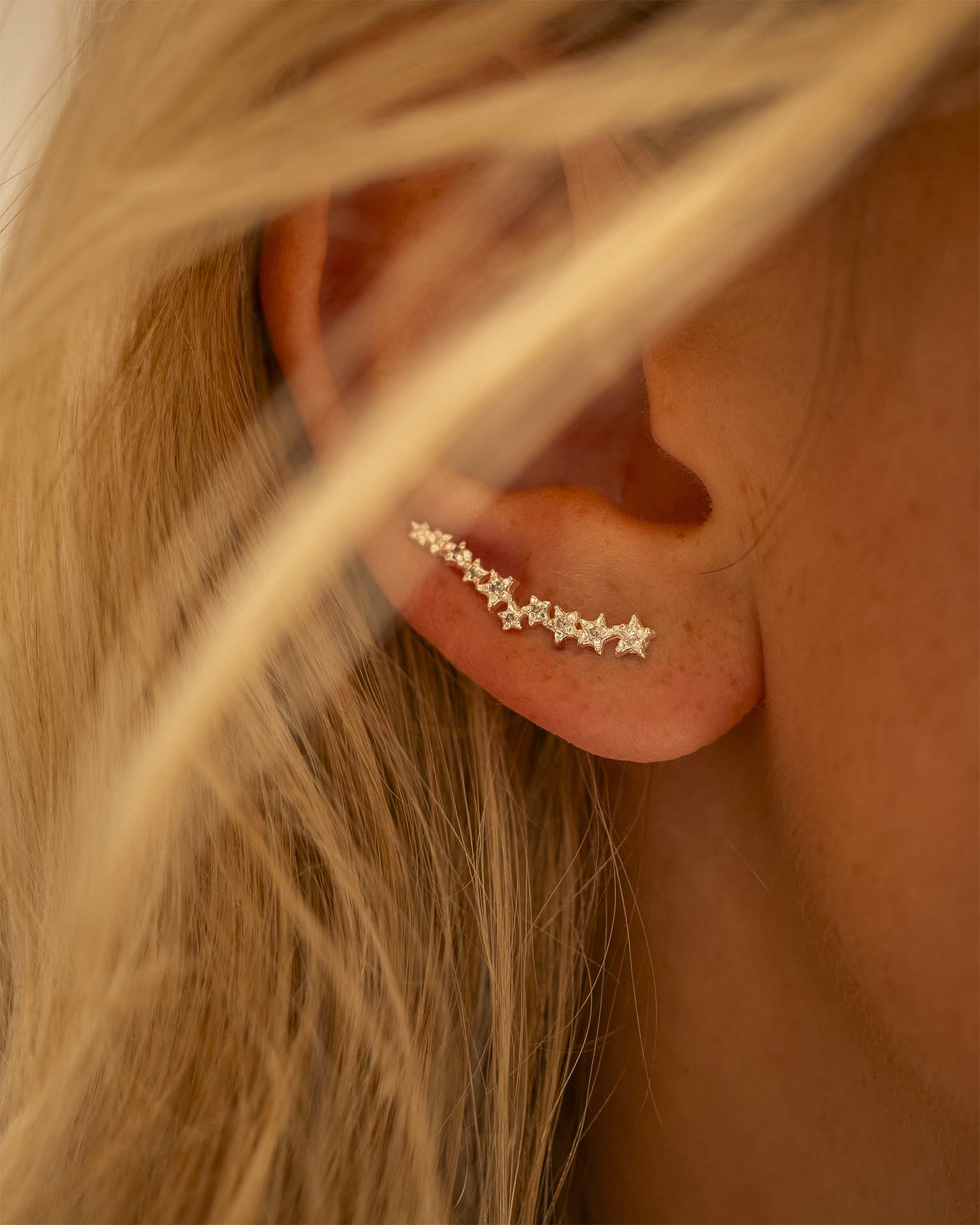 Close-up of an ear wearing a star-shaped earring with blonde hair in the foreground. | Christmas