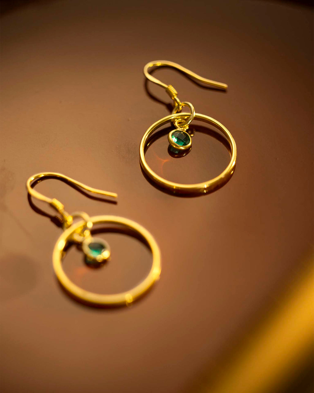 Gold hoop earrings with green gemstones on a brown surface