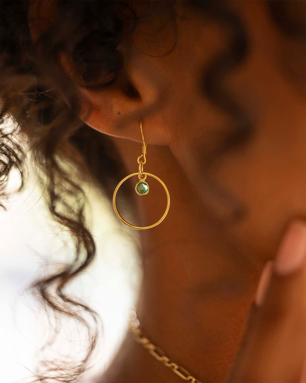 Close-up of a person wearing gold hoop earrings with a green gemstone. | Christmas