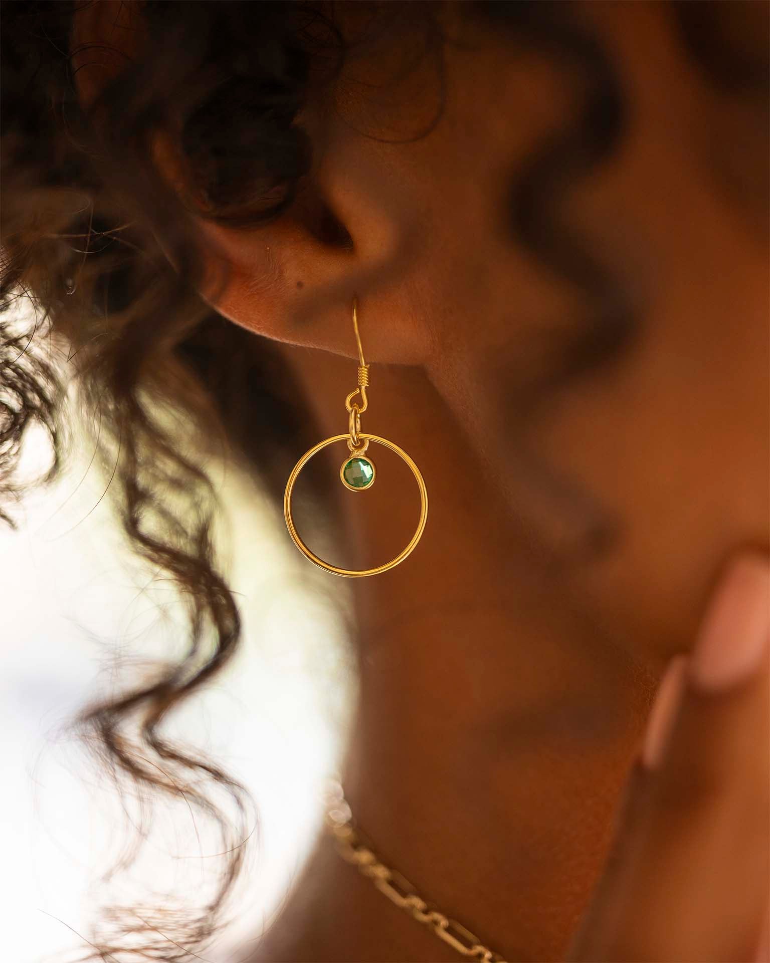 Close-up of a person wearing gold hoop earrings with a green gemstone. | Christmas